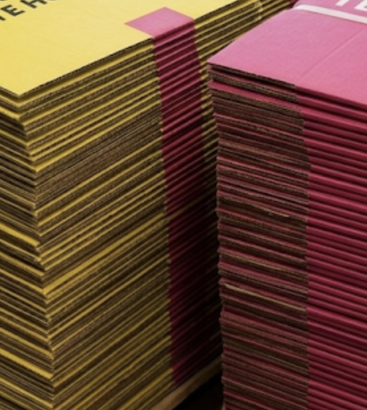Close-up van platgevouwen gele en roze Deel-Doos verhuisdozen, netjes opgestapeld